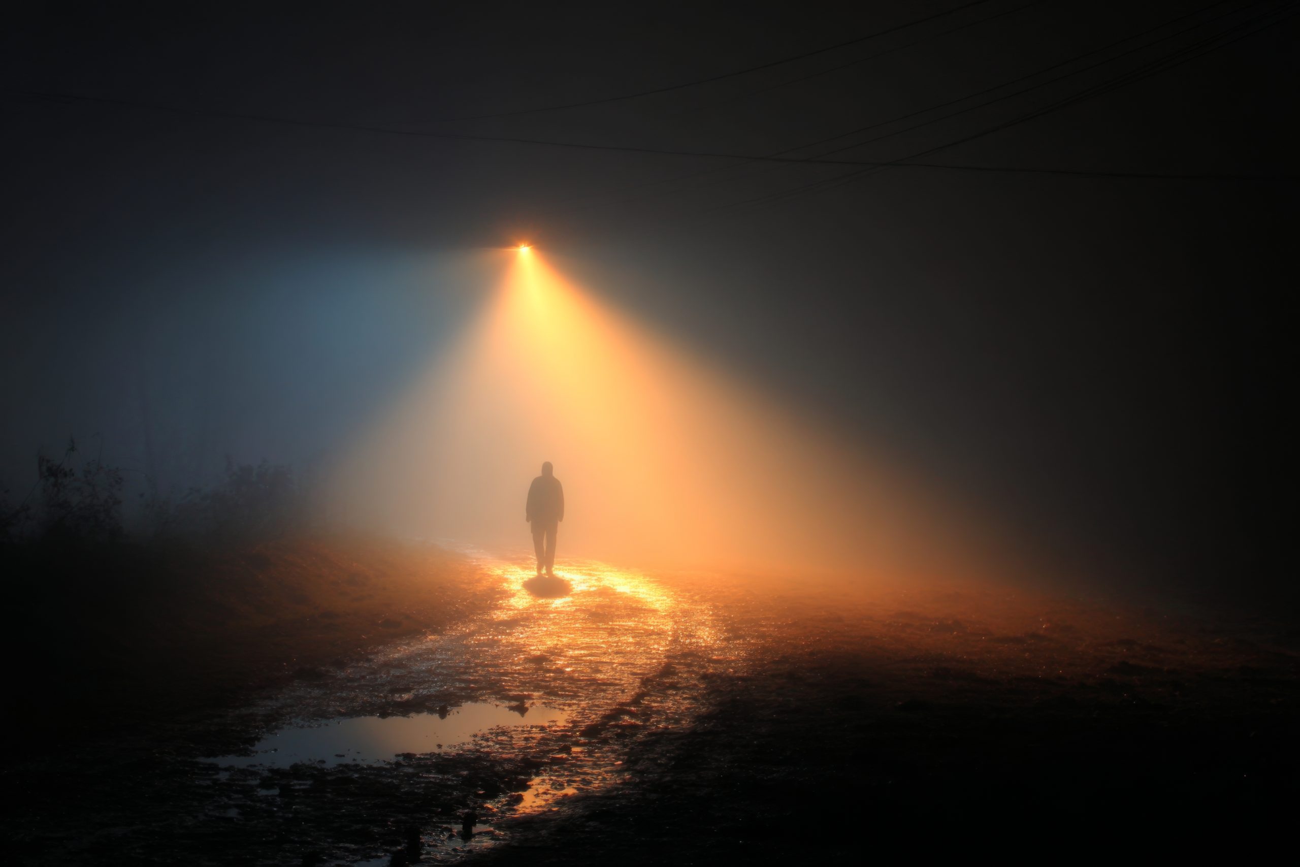 Lone person walking on a muddy path through thick fog illuminate